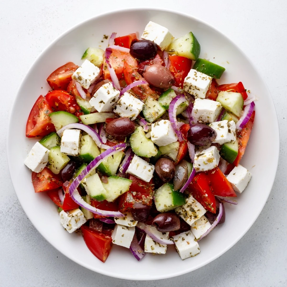 Freshly tossed Mediterranean Salad, featuring juicy tomatoes, cucumbers, and briny olives, drizzled with olive oil.