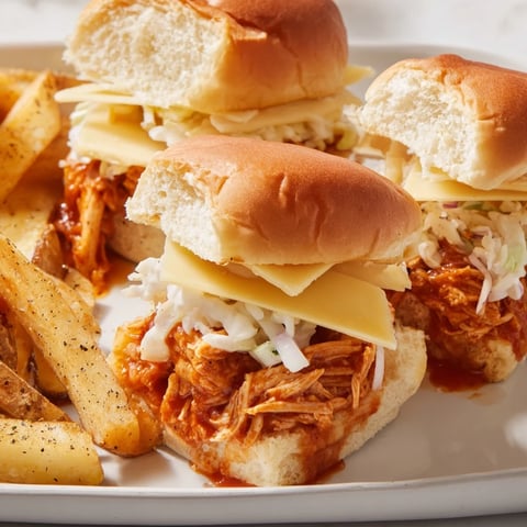 Juicy BBQ Chicken Sliders topped with crunchy coleslaw and served with fries.  