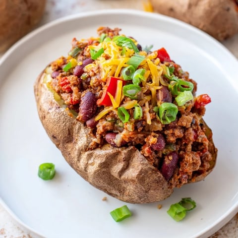 Steaming Chili-Style Baked Potatoes, loaded with a rich chili, cheese, and fresh green onions, look appetizing.