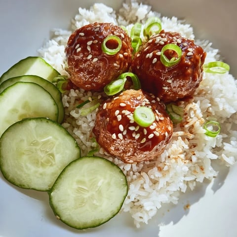 Juicy teriyaki meatball bowls with glistening sauce, rice, cucumber, and sprinkled sesame seeds ready to be enjoyed.