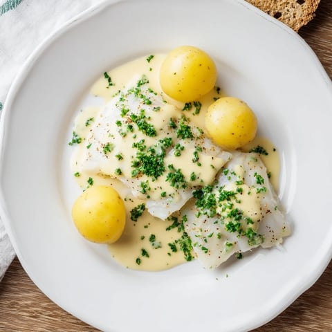 Flaky Norwegian Lutefisk with creamy mustard sauce, served with potatoes and crispbread for a festive meal.