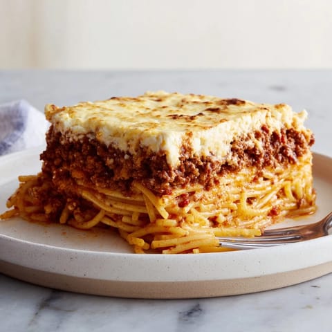 Layers of rich Greek Pastitsio featuring ground beef, pasta, and golden cheese sauce.  