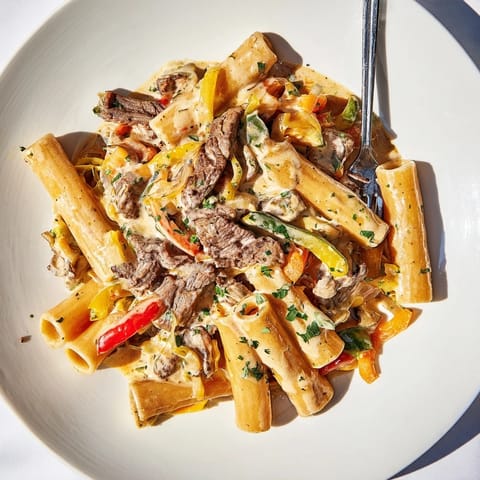 Creamy Philly Cheese Steak Pasta garnished with fresh parsley and colorful sautéed vegetables.  