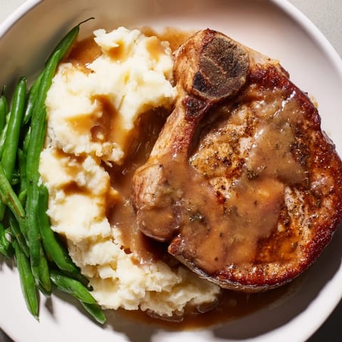 Close-up of golden-brown Pork Chops & Cheddar Mash Bowl with rich gravy and vibrant green beans.