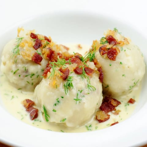 Golden, oval-shaped Cepelinai dumplings, ready to be enjoyed with flavorful bacon and sour cream sauce.