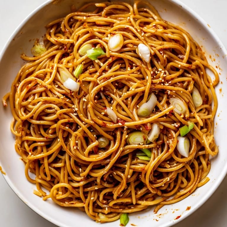 Close-up of vibrant Garlic Chili Oil Noodles, sizzling with chili flakes and fresh scallions served.